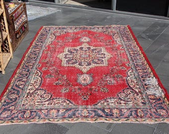 May include: A rectangular, distressed red rug with an intricate floral pattern. The rug features a central medallion design in cream, blue, and gold, surrounded by a navy blue border with floral motifs. The rug is placed on a dark gray surface.