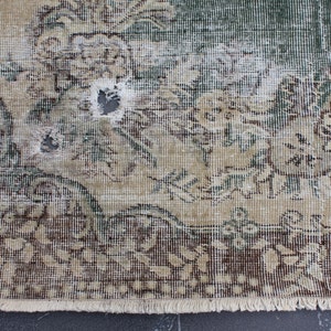 May include: A vintage rug with a floral pattern in shades of brown, green, and white. The rug has a fringe border and shows signs of wear and tear, including a hole in the center.