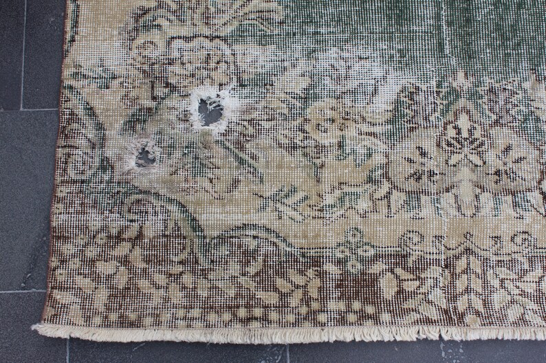 May include: A vintage rug with a floral pattern in shades of brown, green, and white. The rug has a fringe border and shows signs of wear and tear, including a hole in the center.