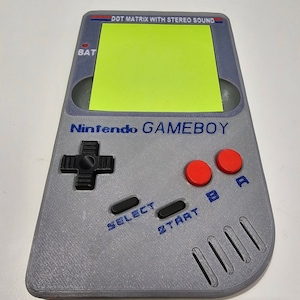 May include: A grey and black Game Boy handheld video game console with a yellow screen. The console has a black directional pad, two black buttons labelled "SELECT" and "START", and two red buttons labelled "A" and "B". The text "DOT MATRIX WITH STEREO SOUND" and "Nintendo GAMEBOY" are printed on the console.