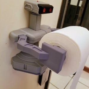 May include: A 3D printed toilet paper holder shaped like a robot from the classic video game, "Metroid". The robot is holding a roll of white toilet paper.