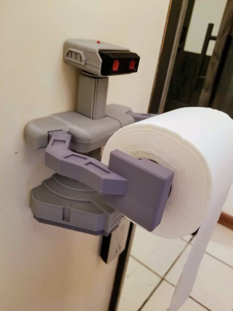 May include: A 3D printed toilet paper holder shaped like a robot from the classic video game, "Metroid". The robot is holding a roll of white toilet paper.