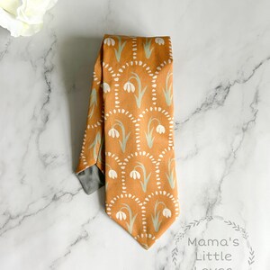 May include: A brown tie with a white and green floral pattern. The tie has a gray lining and is folded in half.