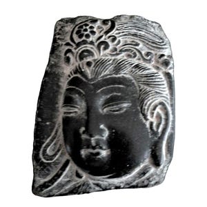 May include: A black stone carving featuring a relief portrait of a serene face with closed eyes and detailed hair ornamentation. The surface displays intricate etched lines and a smooth finish, capturing the facial features in a dark, matte stone.
