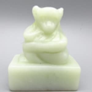 May include: A small, white jade sculpture of a monkey sitting on a square base. The monkey is holding its hands together in front of its chest.
