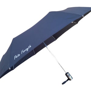 May include: A dark blue umbrella with a silver handle and a white inscription that reads "Pete Forsyth".
