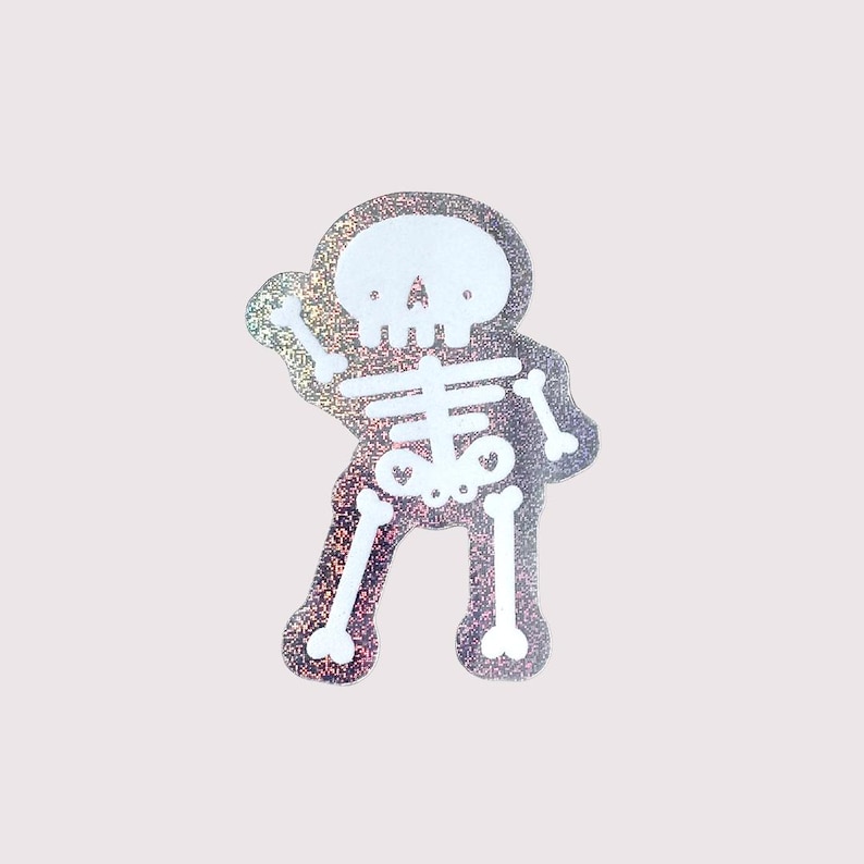 May include: A die-cut sticker featuring a white skeleton illustration with a holographic, glittery background. The skeleton is depicted in a standing pose with arms slightly raised, showcasing a simple, bold graphic design with clear outlines.