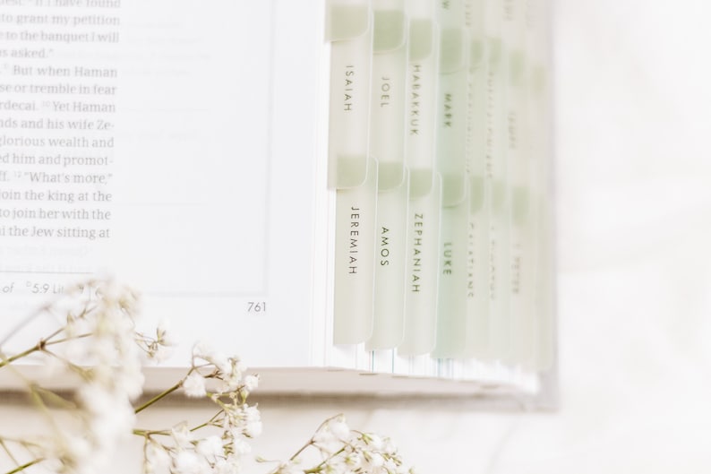 Op de afbeelding: Een close-up van een wit boek met groene tabs met de namen van boeken uit de Bijbel, waaronder Jesaja, Jeremia, Amos, Zefanja, Jo&euml;l, Habakuk, Markus, Lucas en anderen.