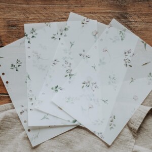Puede incluir: Cinco hojas de papel transl&uacute;cido con un delicado patr&oacute;n floral impreso en tonos verdes y morados. El papel tiene agujeros a lo largo del lado para su uso en una carpeta.