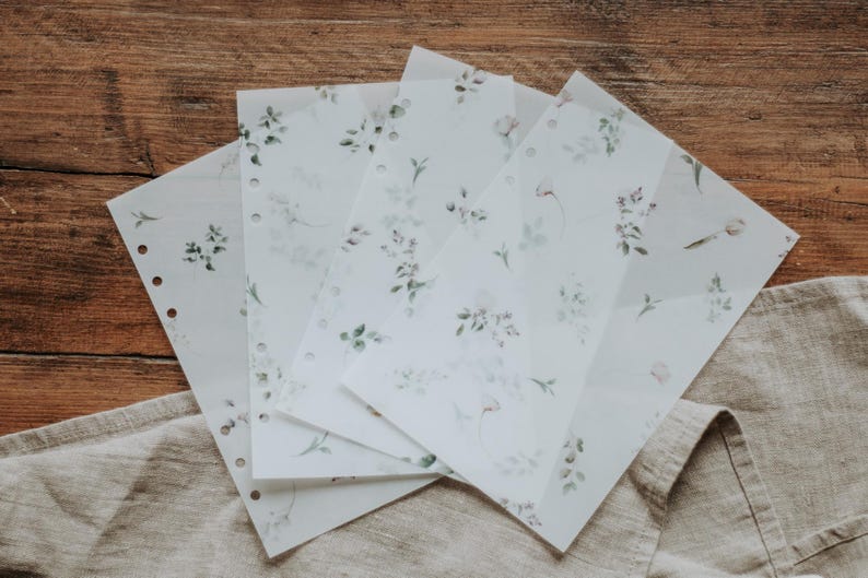 Puede incluir: Cinco hojas de papel transl&uacute;cido con un delicado patr&oacute;n floral impreso en tonos verdes y morados. El papel tiene agujeros a lo largo del lado para su uso en una carpeta.