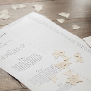 May include: A white sheet of paper with instructions for a game called "Appointed". The instructions are numbered one to five. There are small white paper shapes with numbers on them scattered on the paper. The paper is on a wooden surface.