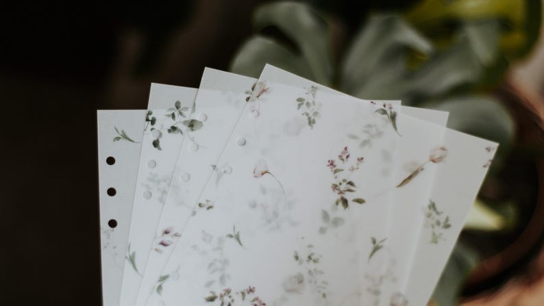 Puede incluir: Un conjunto de cuatro hojas de papel blancas, transl&uacute;cidas, con estampado floral y agujeros perforados en el borde izquierdo. Las hojas son ligeramente transl&uacute;cidas y tienen un delicado dise&ntilde;o floral en tonos verdes y rosas.