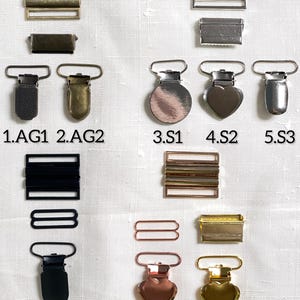 May include: An assortment of metal hardware components, including rectangular sliders, rectangular buckles, and suspender clips. The clips come in various shapes, including round, heart, and rectangular, and in colors like silver, gold, and black.