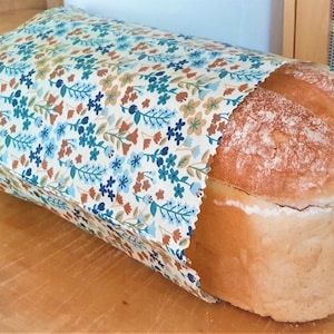 May include: A loaf of white bread wrapped in a floral patterned reusable food wrap. The wrap has a white background with blue, brown, and tan flowers and leaves.