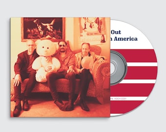 May include: CD case and disc featuring a band photo and album title "Out in America." The case shows four people seated on a couch with a teddy bear. The disc has red and white stripes.