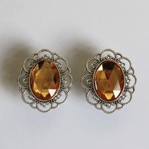 May include: A pair of silver earrings with a filigree design and a large oval amber-colored gemstone in the center.