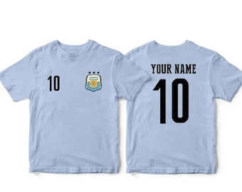 May include: Light blue t-shirt with the number 10 on the front and back. The front also features the Argentina national soccer team crest. The back of the shirt has the text "YOUR NAME" above the number 10.