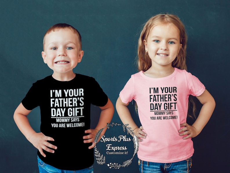 May include: Two children wearing t-shirts with the text "I'm your Father's Day Gift. Mommy says you are welcome!" One child is wearing a black t-shirt and the other is wearing a pink t-shirt.
