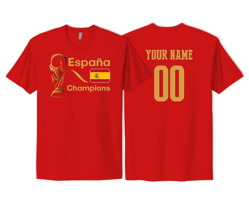 May include: A red short-sleeved t-shirt featuring a gold trophy graphic, the text Espa&ntilde;a Champions, and a Spanish flag on the front. The back displays the text YOUR NAME in gold above the gold numbers 00, centered on the red fabric.