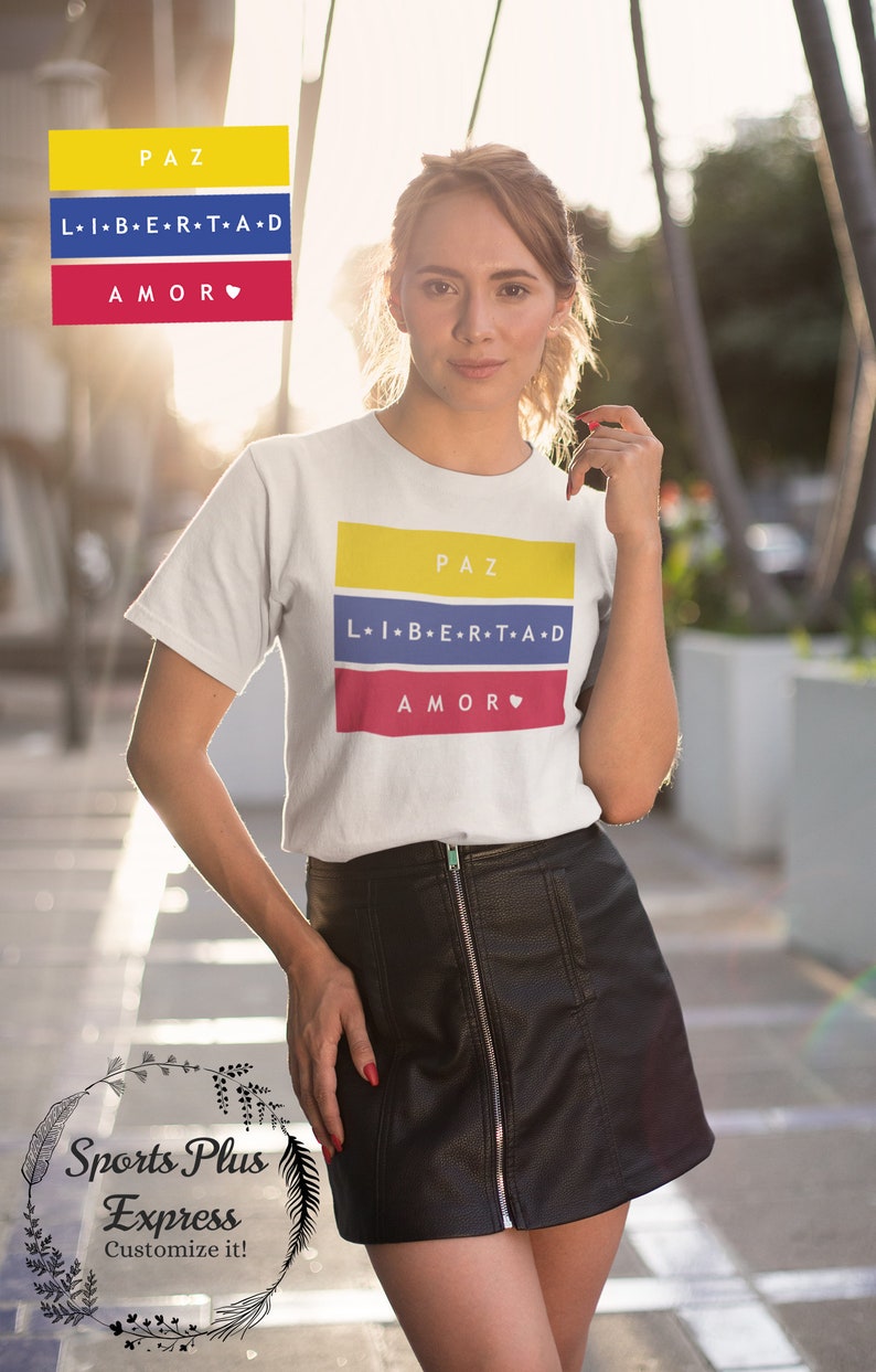 Pu&ograve; includere: Una maglietta bianca con un design grafico con i colori della bandiera colombiana. La grafica include le parole "PAZ", "LIBERTAD" e "AMOR" in spagnolo. La maglietta &egrave; indossata da una persona con una gonna di pelle nera.