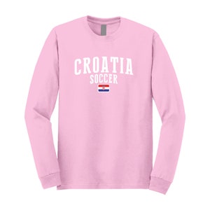 May include: Pink long-sleeve t-shirt with white text that reads "CROATIA SOCCER" and a small Croatian flag.
