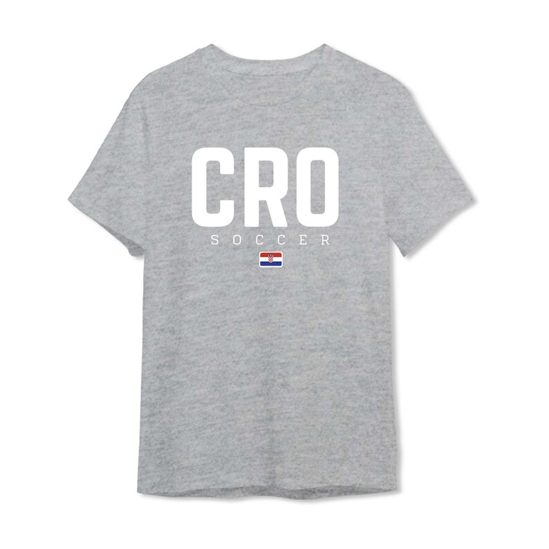 以下が含まれることがあります： 大きな白い文字で「CRO」と書かれた、ヘザーグレーのTシャツ。その下に「SOCCER」の文字と小さなクロアチアの国旗があります。このTシャツはクルーネックです。