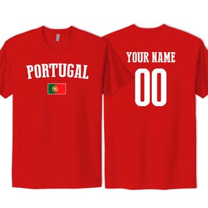May include: A red short-sleeved t-shirt featuring the word PORTUGAL in white arched text above a small Portuguese flag on the front. The back of the shirt displays the text YOUR NAME in white above the large white numbers 00 in a block font.