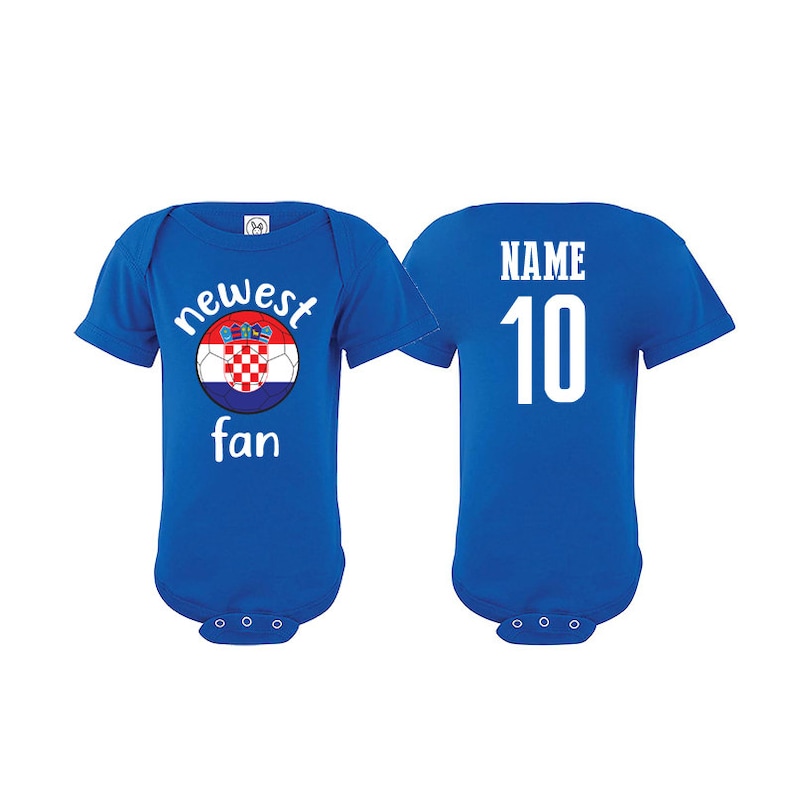 Może przedstawiać: Jasnoniebieski śpioszek dla niemowlęcia z piłką nożną z chorwacką flagą i napisem "newest fan". Z tyłu śpioszka znajduje się napis "NAME 10" w kolorze białym.