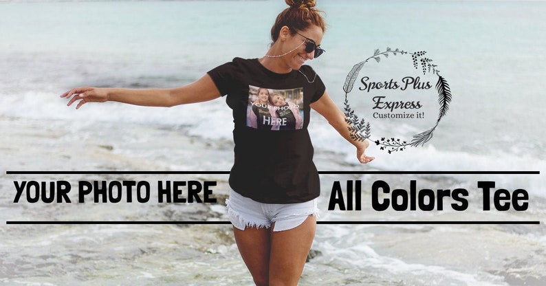 May include: A woman wearing a black t-shirt with a photo of two people on it. The t-shirt says "Your Photo Here" and is available in all colors. The text "Sports Plus Express Customize it!" is on a wreath with leaves.