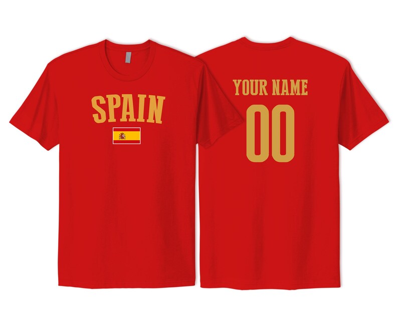 May include: A red short-sleeved t-shirt showing the front and back views. The front features the word SPAIN in gold letters above the Spanish flag. The back displays the text YOUR NAME in gold above the gold numbers 00.