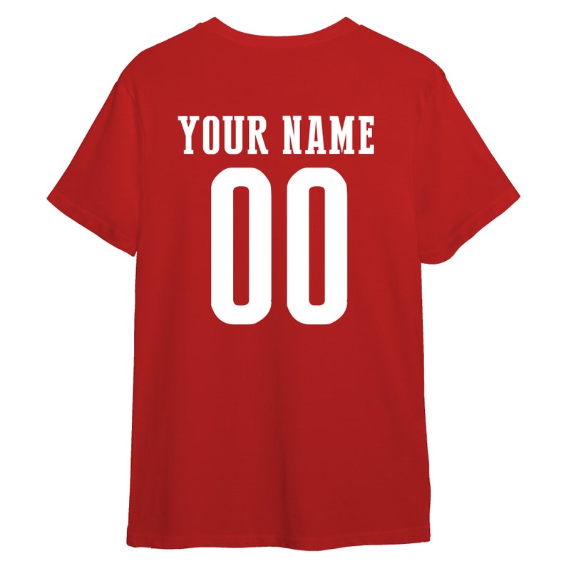 以下が含まれることがあります： 赤色のTシャツ。白で「YOUR NAME」の文字と数字の「00」がプリントされています。Tシャツは無地の赤色で、半袖です。