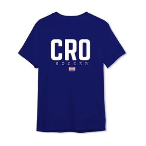 以下が含まれることがあります： 紺色のTシャツ。大きな白い文字で「CRO」と書かれています。その下に「SOCCER」の文字と小さなクロアチア国旗がプリントされています。クルーネックのクラシックなデザインです。