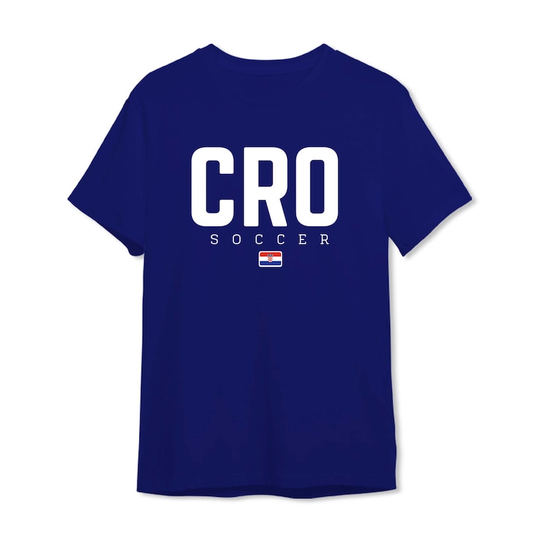 以下が含まれることがあります： 紺色のTシャツ。大きな白い文字で「CRO」と書かれています。その下に「SOCCER」の文字と小さなクロアチア国旗がプリントされています。クルーネックのクラシックなデザインです。