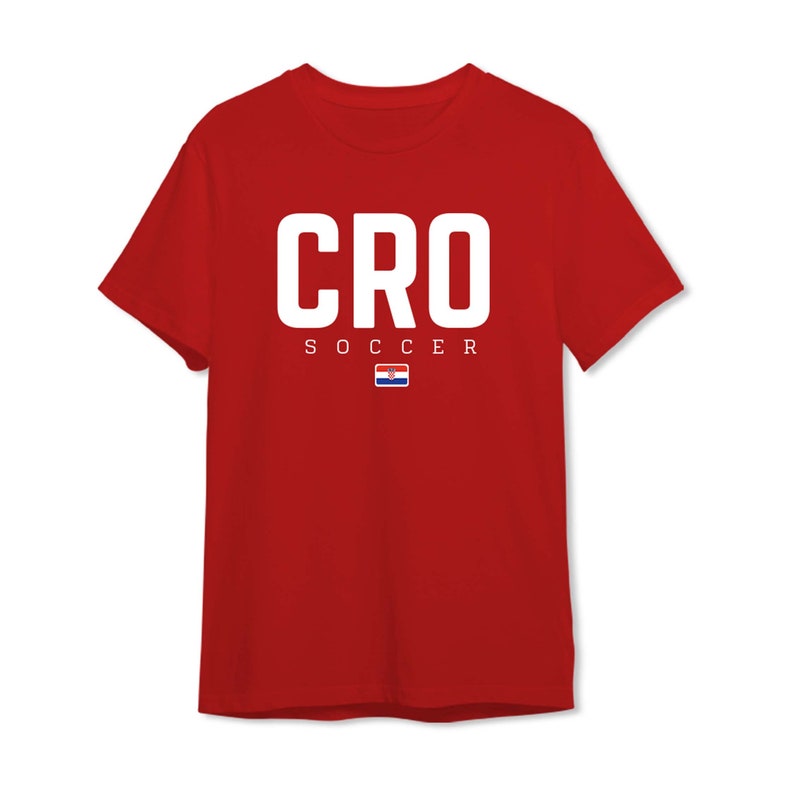 以下が含まれることがあります： 赤いTシャツ。大きな白い文字で「CRO」と書かれ、その下に「SOCCER」と書かれています。小さなクロアチアの国旗が「SOCCER」の下にあります。このシャツはクルーネックです。
