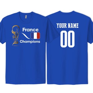 May include: A royal blue t-shirt featuring a gold trophy graphic, the text France Champions, and a French flag on the front. The back displays the text YOUR NAME above the number 00 in white lettering. The shirt has short sleeves and a crew neck.