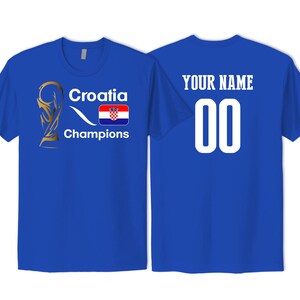 May include: A royal blue t-shirt featuring a gold trophy graphic, the text Croatia Champions, and the Croatian flag on the front. The back of the shirt displays the text YOUR NAME above the number 00 in large white font.