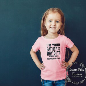 May include: A pink t-shirt with black text that reads "I'm your father's day gift. Mommy says you are welcome!"