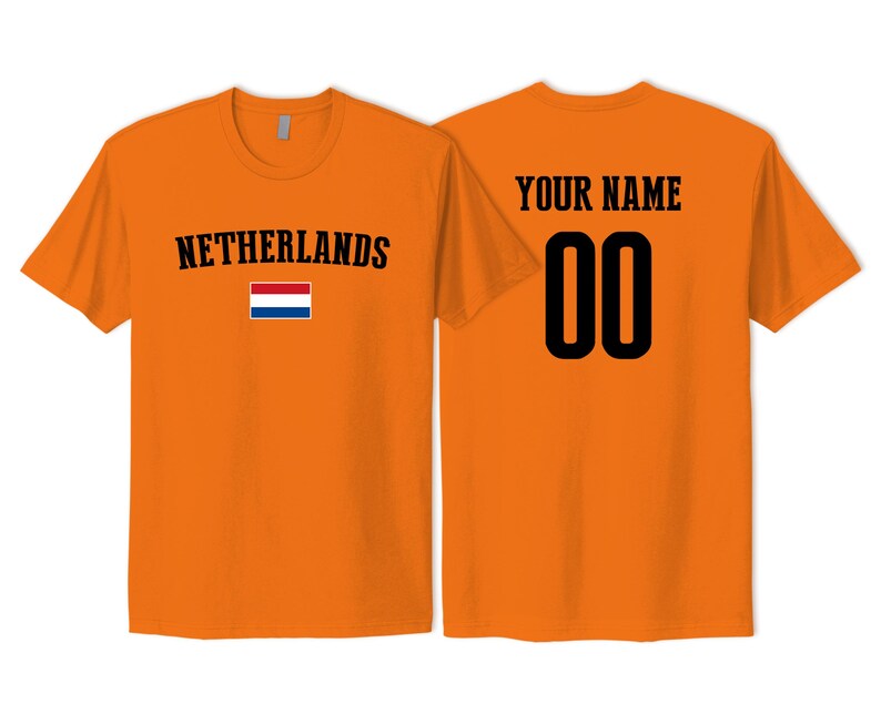 May include: An orange short-sleeved t-shirt featuring the text NETHERLANDS and a small Dutch flag on the front. The back of the shirt displays the text YOUR NAME above the large black numbers 00 in a bold, athletic-style font.