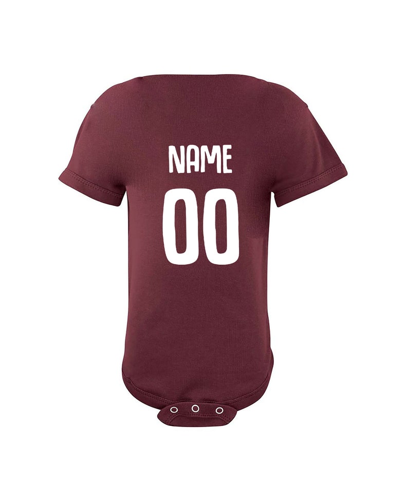 May include: Burgundy baby bodysuit with white text that says "NAME 00" on the back.