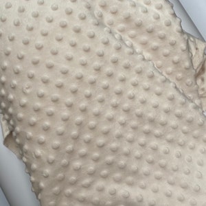 May include: Close-up of a cream-coloured fabric with a textured, raised dot pattern. The fabric is soft and plush.