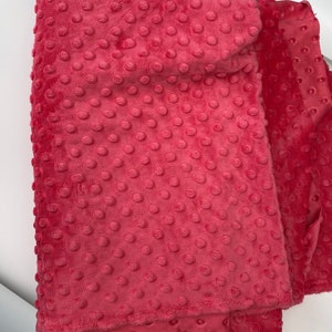 May include: A close-up of a pink minky fabric with a textured dot pattern. The fabric is soft and plush, ideal for blankets, baby clothes, and other crafts.