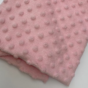 May include: A close-up of a soft, pink fabric with a textured, dotted pattern. The fabric is folded in half, showing the texture of the dots.