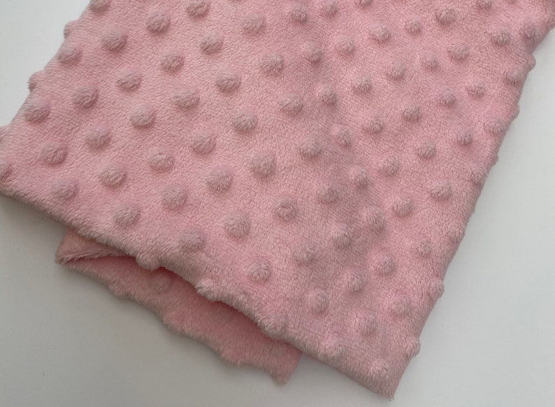 May include: A close-up of a soft, pink fabric with a textured, dotted pattern. The fabric is folded in half, showing the texture of the dots.