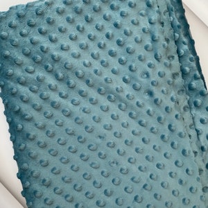 May include: A close-up of a soft, blue fabric with a textured, dotted pattern. The fabric is folded in half, showing the texture of the material.