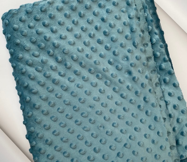 May include: A close-up of a soft, blue fabric with a textured, dotted pattern. The fabric is folded in half, showing the texture of the material.