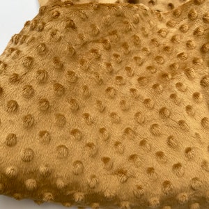May include: A close-up of a soft, brown fabric with a textured, dotted pattern. The fabric has a fuzzy, plush feel.
