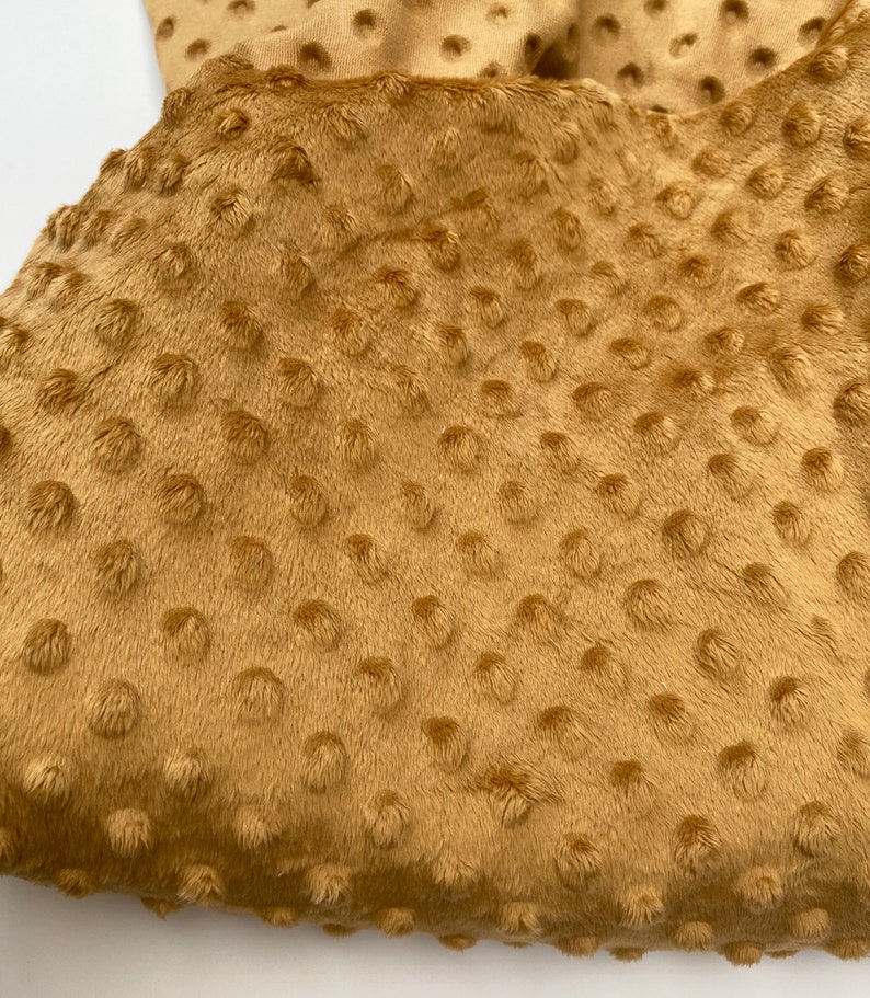 May include: A close-up of a soft, brown fabric with a textured, dotted pattern. The fabric has a fuzzy, plush feel.