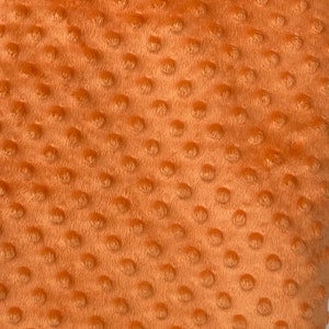 May include: Close-up of a soft, orange fabric with a textured, dotted pattern. The fabric is plush and has a fuzzy texture.