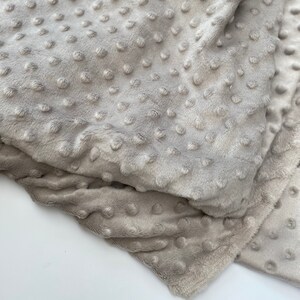 May include: A soft, grey, textured fabric with a subtle dot pattern. The fabric is folded and appears to be a plush material.
