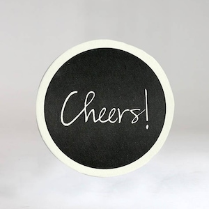 May include: A round black coaster with a white border and the word "Cheers!" written in white script.